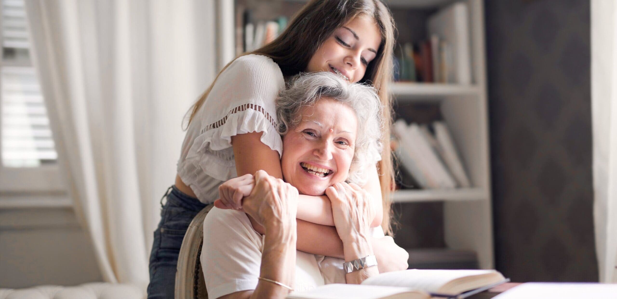 young lady with arms around elderly woman's neck embracing her