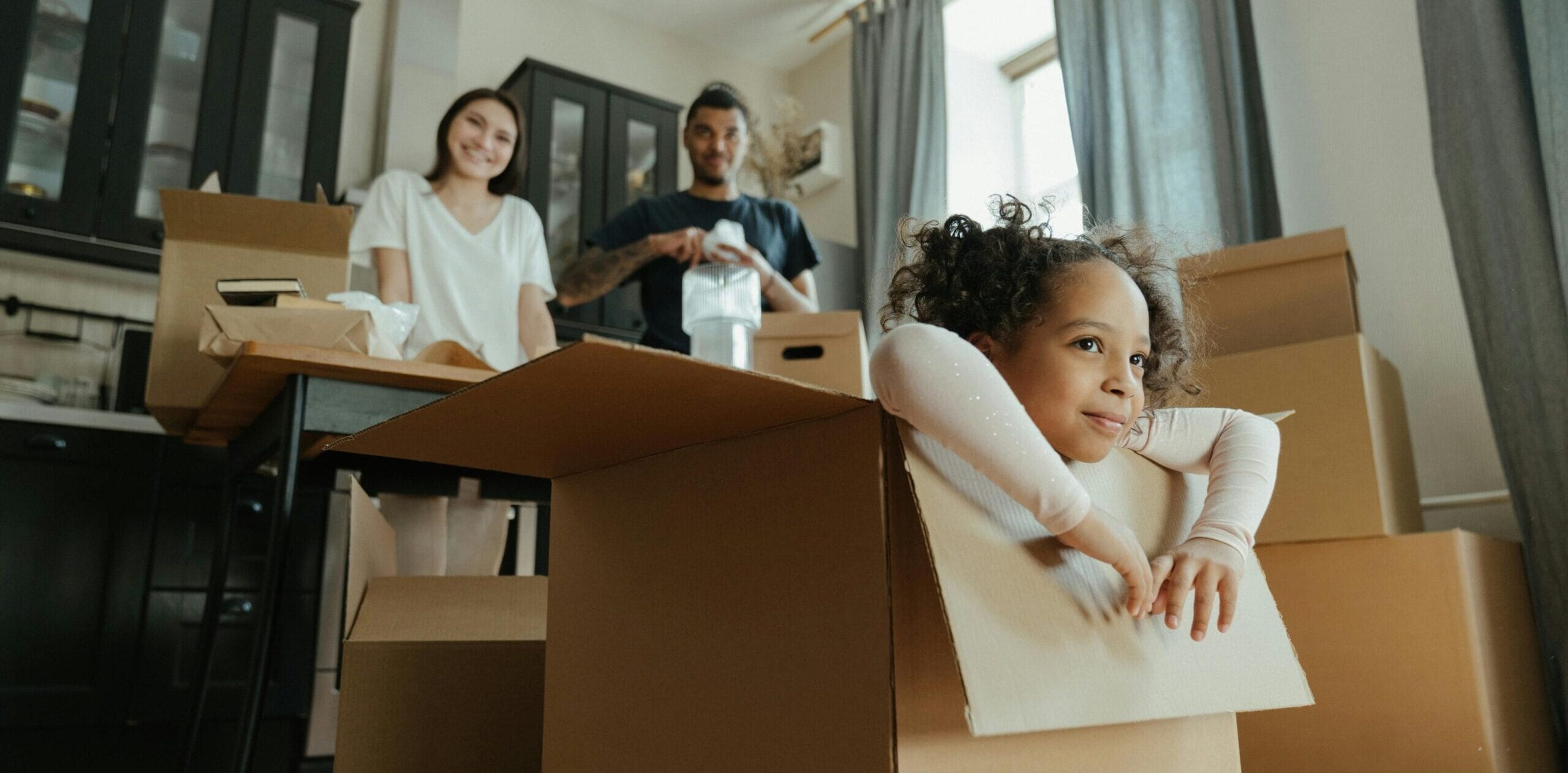 little girl sitting in moving box with man and woman looking on behind