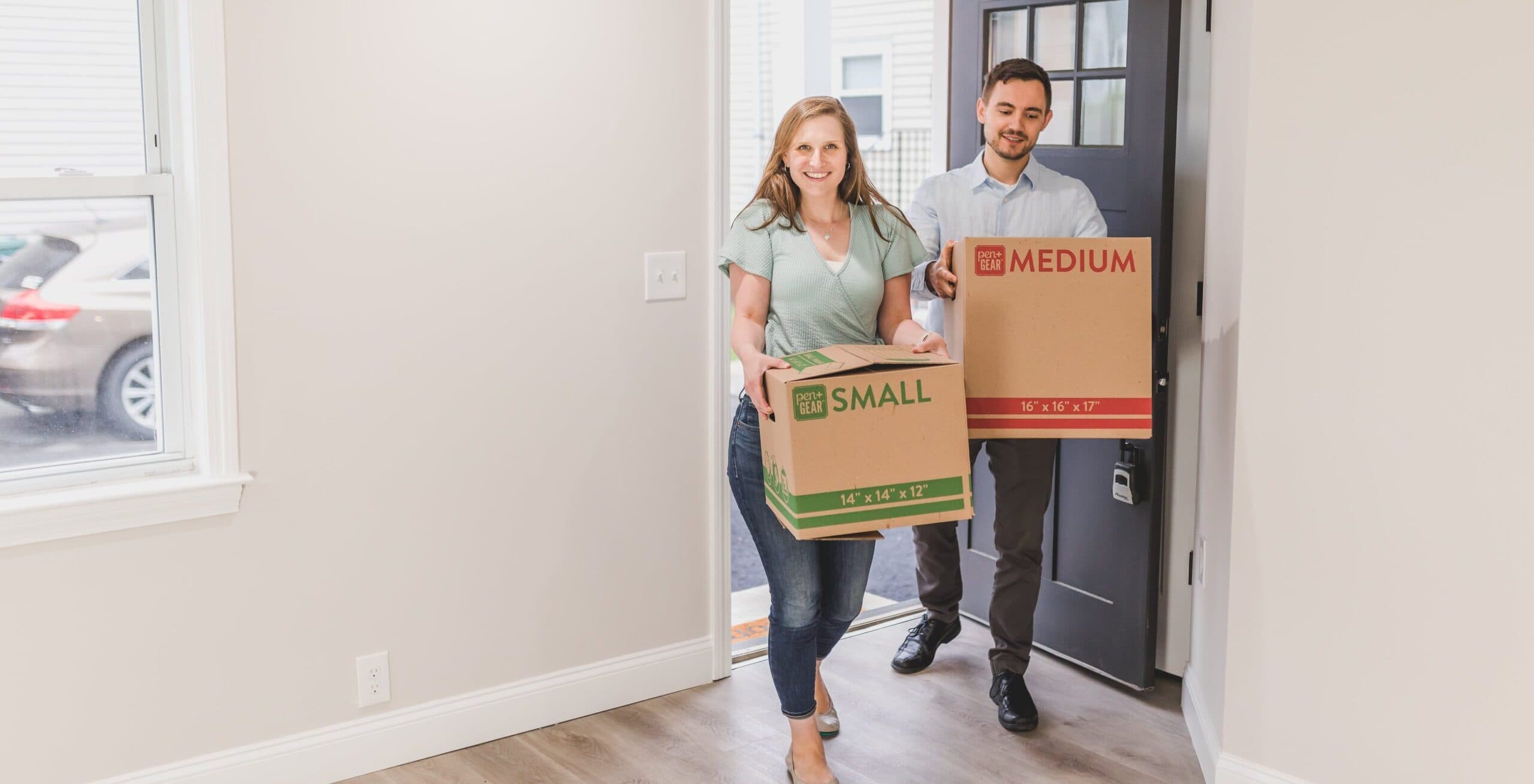 man and woman coming into empty home carrying boxes